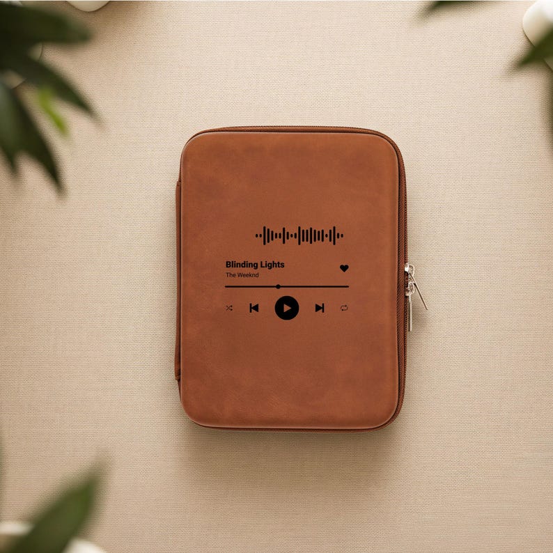 May include: A brown tablet case with a zipper closure. The case features a graphic of a song's waveform, play controls, and the text "Blinding Lights" by The Weeknd.