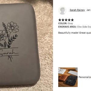 May include: Gray leather cord case with a floral design and the name "Sarah" engraved. The case is rectangular with rounded corners and a zipper closure. The floral design includes two large flowers and other foliage.