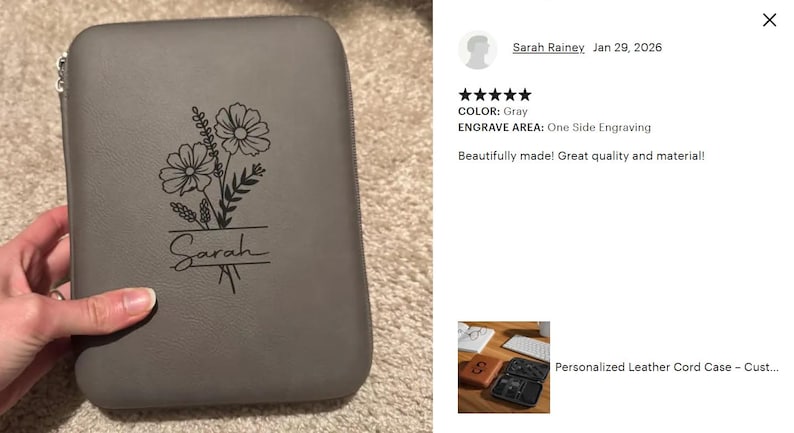 May include: Gray leather cord case with a floral design and the name "Sarah" engraved. The case is rectangular with rounded corners and a zipper closure. The floral design includes two large flowers and other foliage.