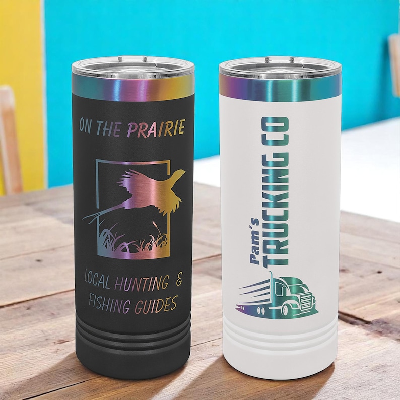 May include: Two insulated tumblers with iridescent rims. One black tumbler features a pheasant graphic and text reading "ON THE PRAIRIE" and "LOCAL HUNTING & FISHING GUIDES." The other is white with "Pam's TRUCKING CO" and a truck graphic.