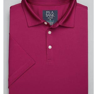 May include: A solid magenta short-sleeve polo shirt with a button-down collar. The shirt has a J.S.A. Bank label with the text "Traveler" and "Tailored Fit" on it.
