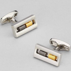 May include: A pair of silver cufflinks with a gold and silver design. The cufflinks are rectangular in shape and have a small, decorative detail in the center.