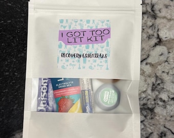 May include: A white pouch with a clear window containing recovery essentials. The pouch has a label that reads "I GOT TOO LIT KIT" and "RECOVERY ESSENTIALS." Visible items include electrolyte drink mix, and gum.