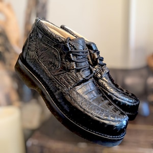 May include: A pair of black leather ankle boots with a crocodile skin texture. The boots have a lace-up design and a thick sole. The shoes are approximately 6 inches tall.
