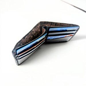 Op de afbeelding: Een zwarte leren portemonnee met een bruine su&egrave;de binnenkant. De portemonnee is open en bevat verschillende creditcards, waaronder een American Express kaart en een PNC Bank kaart.