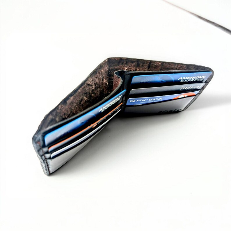 Op de afbeelding: Een zwarte leren portemonnee met een bruine su&egrave;de binnenkant. De portemonnee is open en bevat verschillende creditcards, waaronder een American Express kaart en een PNC Bank kaart.