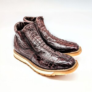 May include: A pair of brown leather boots with a crocodile skin pattern and a zipper on the side. The boots have a white rubber sole.