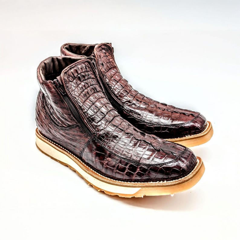 May include: A pair of brown leather boots with a crocodile skin pattern and a zipper on the side. The boots have a white rubber sole.