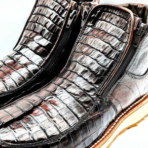 May include: A pair of brown leather boots with a crocodile skin pattern and side zippers. The boots have a thick white sole.
