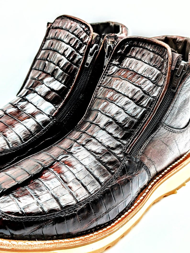 May include: A pair of brown leather boots with a crocodile skin pattern and side zippers. The boots have a thick white sole.