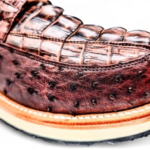 May include: Close-up of a brown leather shoe. The upper features a crocodile pattern, while the sides have an ostrich leather texture. The shoe has a cream sole with a black outsole and orange trim.