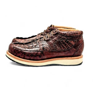 May include: A pair of brown leather boots with a crocodile skin texture. The boots have a lace-up design and a thick, off-white sole. The boots are a size 10, which is approximately a 28 cm foot length.