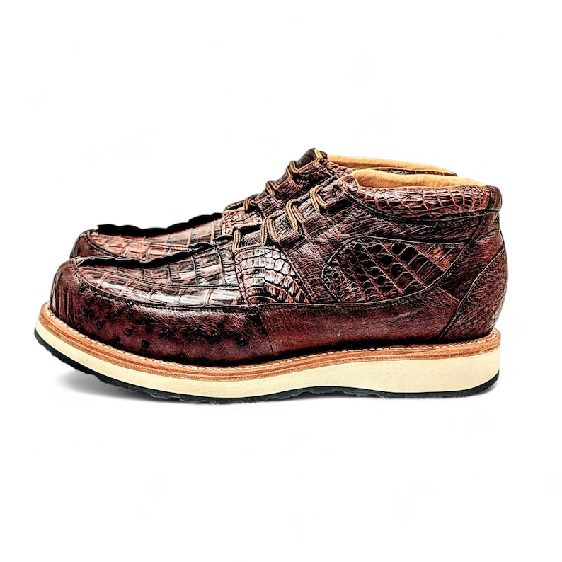 May include: A pair of brown leather boots with a crocodile skin texture. The boots have a lace-up design and a thick, off-white sole. The boots are a size 10, which is approximately a 28 cm foot length.