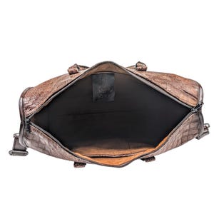 May include: Brown leather duffel bag with a textured crocodile pattern. The bag is open, revealing a black interior. The zipper is silver. A black tag with the text "SOULK" is visible inside the bag.