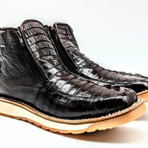 May include: A pair of brown leather boots with a crocodile skin pattern. The boots have a zipper on the side and a white rubber sole.