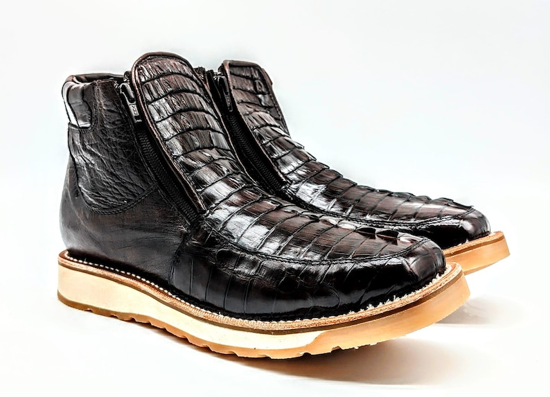 May include: A pair of brown leather boots with a crocodile skin pattern. The boots have a zipper on the side and a white rubber sole.