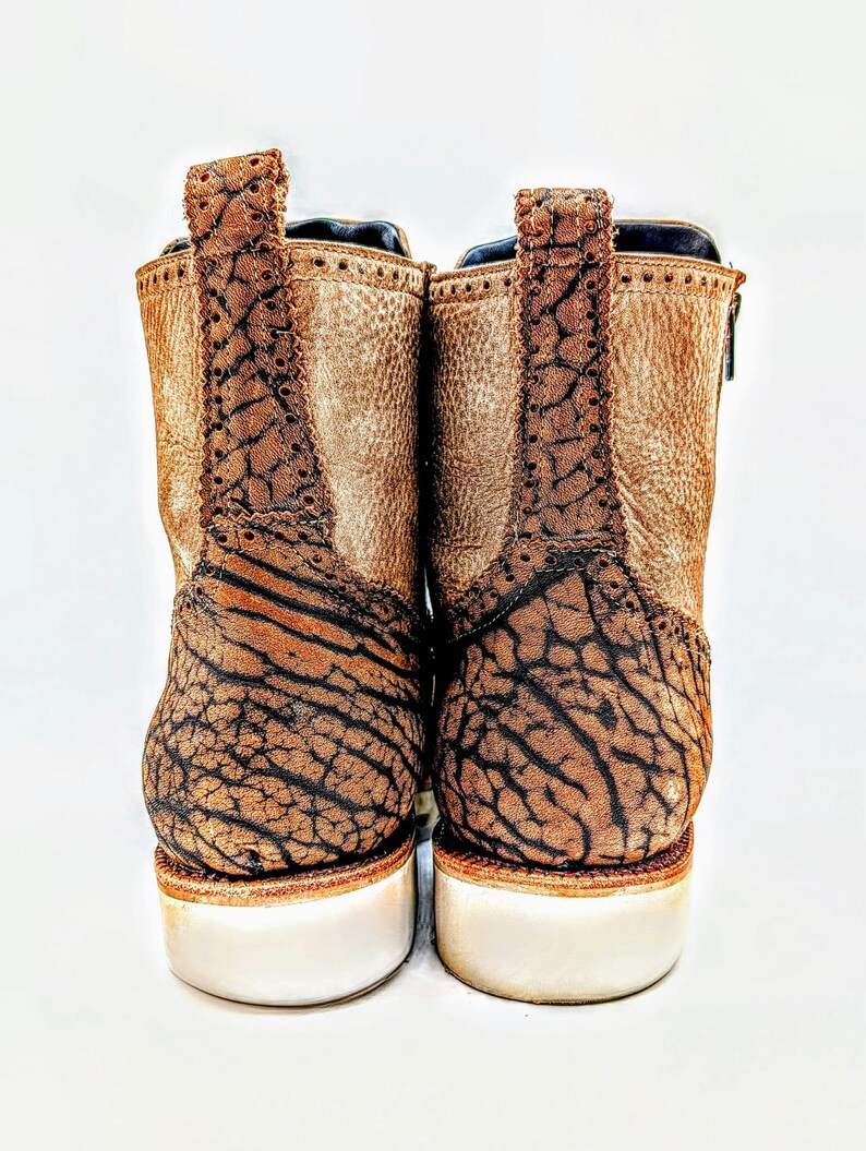 May include: Pair of brown leather ankle boots with a textured design on the back and heel. The boots have a white sole and a pull tab at the top. The leather has a distressed appearance.