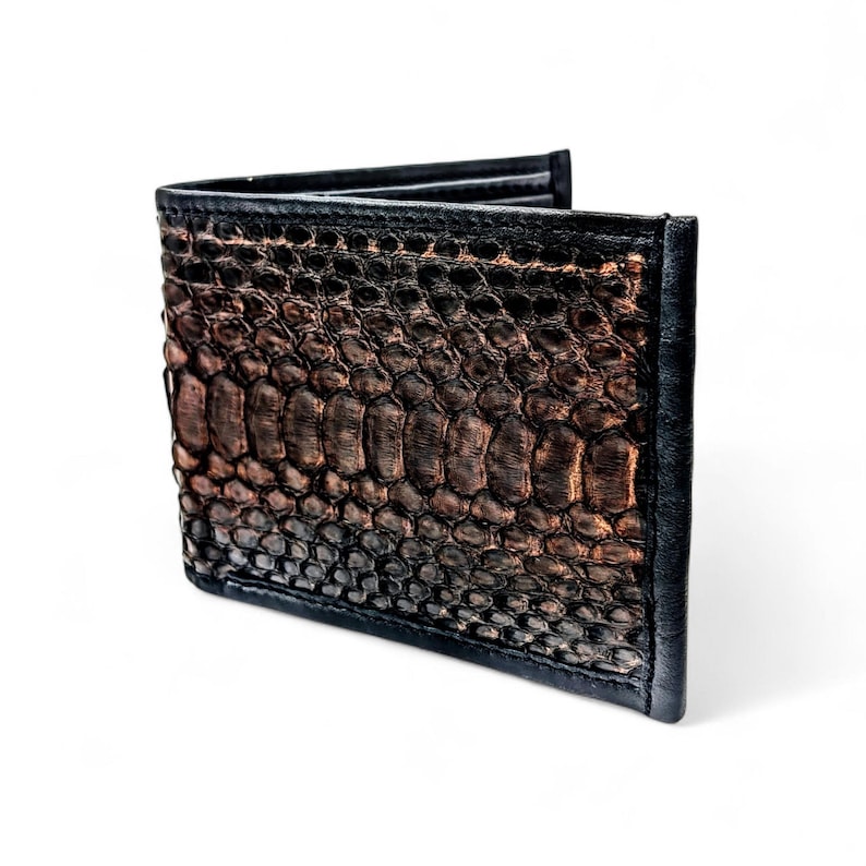 May include: A bi-fold wallet with a textured, reptile-like pattern in shades of brown and black. The wallet has a black border and appears to be made of leather. The design gives the wallet a unique and stylish appearance.