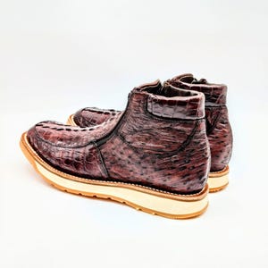 May include: A pair of brown ostrich leather ankle boots with a zipper on the side. The boots have a white rubber sole and a brown leather heel.