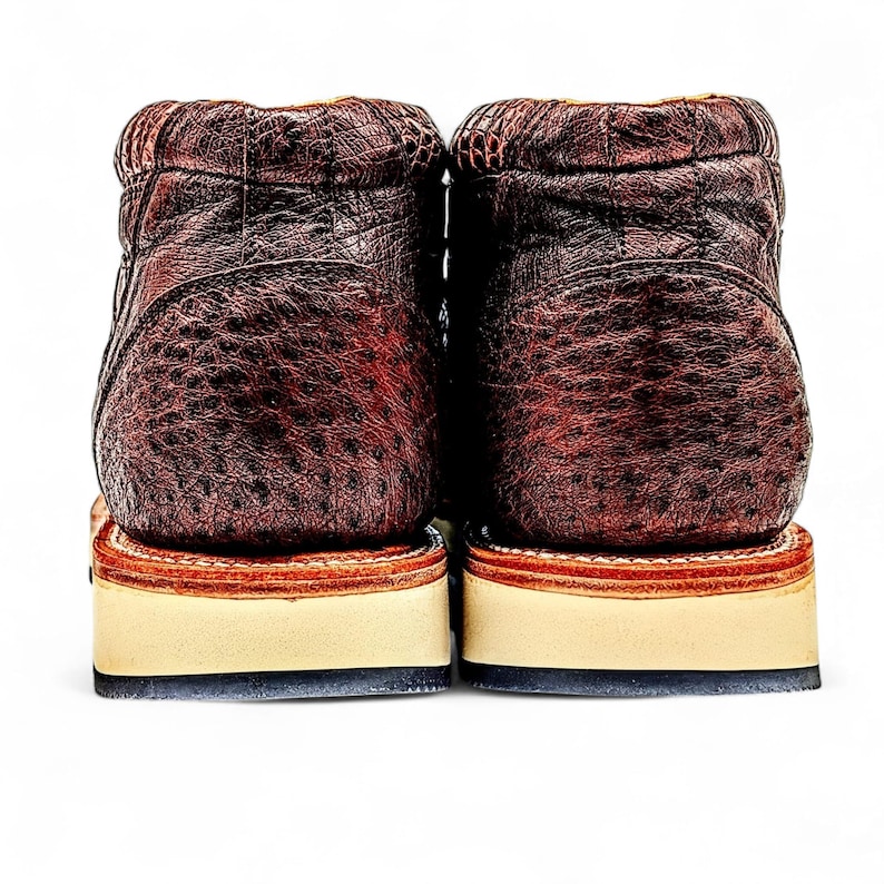 May include: A pair of brown leather boots with a textured finish. The boots feature a stacked sole with a cream base and a dark brown trim. The boots are set against a white background.