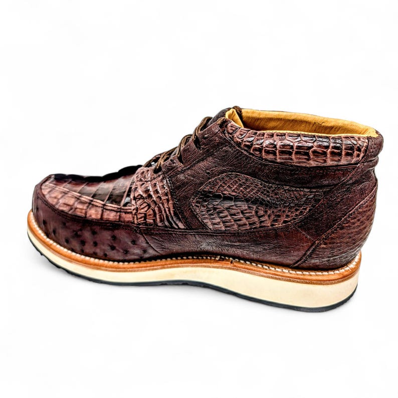May include: A brown leather boot with a crocodile-effect texture. The boot has a rounded toe, lace-up closure, and a thick, off-white sole with a brown trim. The upper is a dark, rich brown. The boot's design suggests a focus on craftsmanship.
