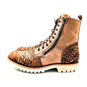 May include: Tan leather boots with a textured, cracked pattern on the toe and heel. The boots have a side zipper, brown laces, and a white sole. The boots are a rugged style.