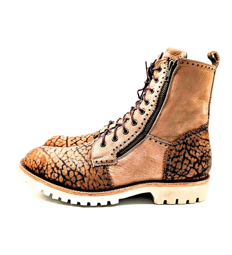 May include: Tan leather boots with a textured, cracked pattern on the toe and heel. The boots have a side zipper, brown laces, and a white sole. The boots are a rugged style.