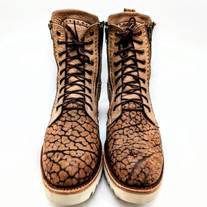 May include: A pair of brown leather boots with a unique cracked pattern design. The boots have laces, side zippers, and white soles. The boots are approximately 8 inches tall.