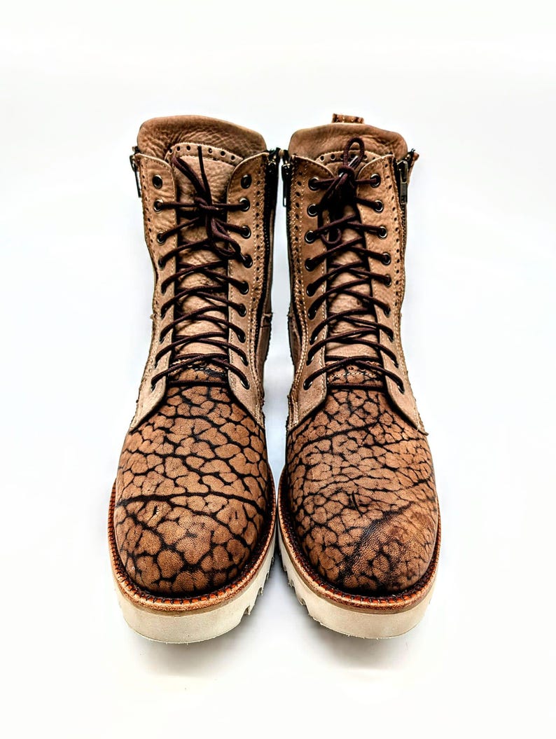 May include: A pair of brown leather boots with a unique cracked pattern design. The boots have laces, side zippers, and white soles. The boots are approximately 8 inches tall.