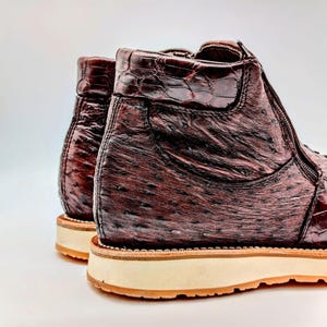 May include: A pair of brown leather boots with a zipper on the side. The boots have a textured ostrich leather upper and a white rubber sole.