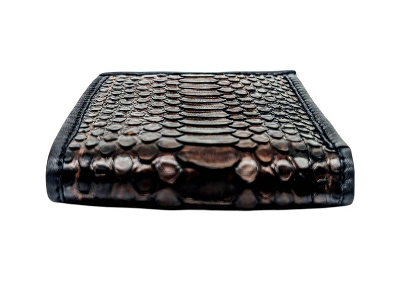 May include: A rectangular wallet with a snakeskin pattern in shades of brown and black. The wallet has a textured surface and a black border. The design is detailed and the overall look is luxurious.