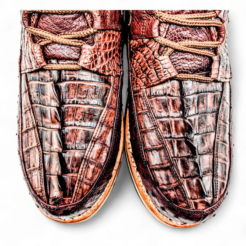 May include: Close-up of two brown leather shoes with a crocodile skin texture. The shoes have tan laces and a light-coloured sole. The leather has a glossy finish and a detailed pattern.