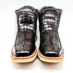 May include: A pair of brown leather boots with a crocodile skin pattern. The boots have a zipper on the side and a white rubber sole.