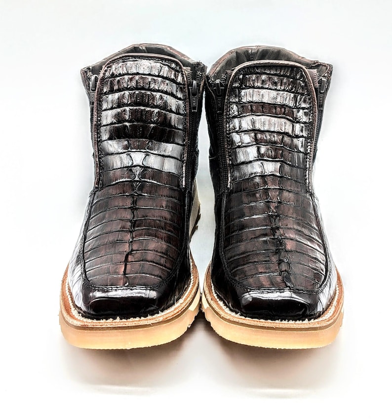 May include: A pair of brown leather boots with a crocodile skin pattern. The boots have a zipper on the side and a white rubber sole.
