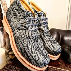 May include: A pair of gray and black leather ankle boots with a textured pattern. The boots have a thick, cream-colored sole and gray laces.