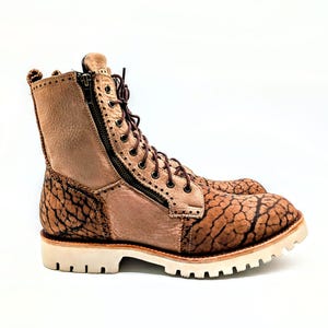 May include: A pair of tan leather boots with a unique textured pattern on the toe and heel. The boots have a side zipper, brown laces, and a white sole. The boots are approximately 8 inches tall.