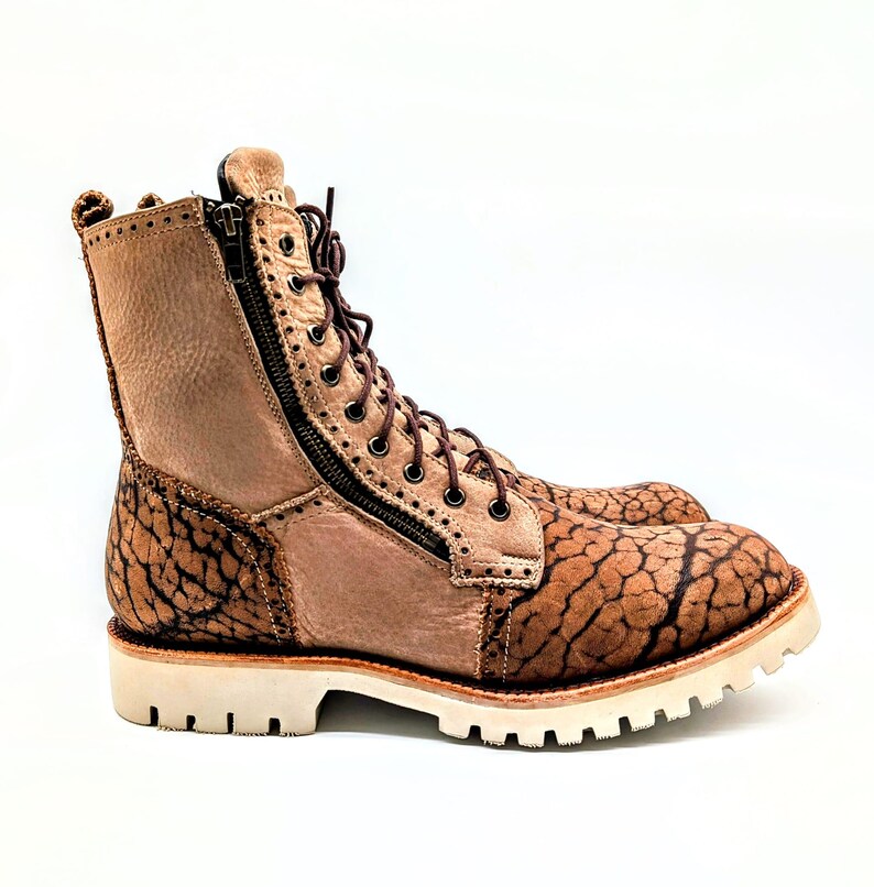 May include: A pair of tan leather boots with a unique textured pattern on the toe and heel. The boots have a side zipper, brown laces, and a white sole. The boots are approximately 8 inches tall.