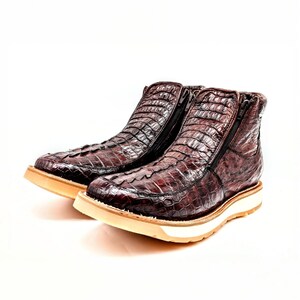 May include: A pair of brown leather boots with a crocodile skin pattern and zipper closures. The boots have a white rubber sole.