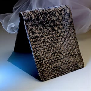 May include: A bi-fold wallet with a textured, reptile-like pattern in shades of brown and gray. The wallet is open, revealing a dark interior. The design gives the wallet a unique, stylish appearance. The wallet is made of a durable material.