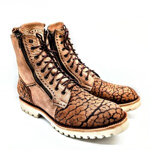 May include: A pair of tan leather boots with a unique cracked pattern on the toe and heel. The boots have a side zipper, brown laces, and a white sole. The boots are approximately 7 inches tall.