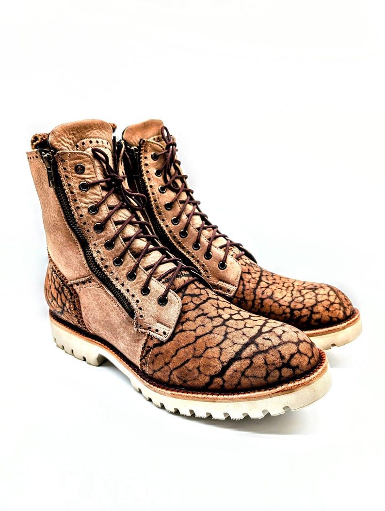 May include: A pair of tan leather boots with a unique cracked pattern on the toe and heel. The boots have a side zipper, brown laces, and a white sole. The boots are approximately 7 inches tall.