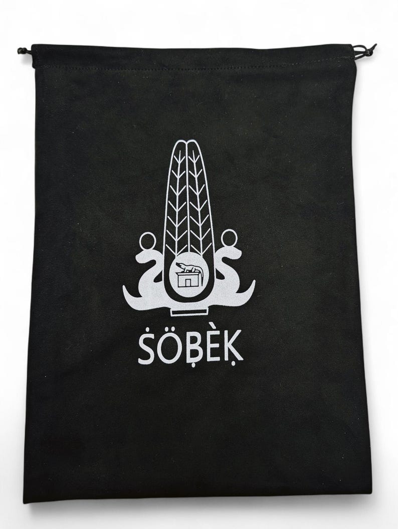 May include: Black drawstring bag with a white emblem and the word "S&Ouml;BEK". The emblem is a stylized design with a central element and flanking curved shapes. The bag is made of a soft, opaque material.