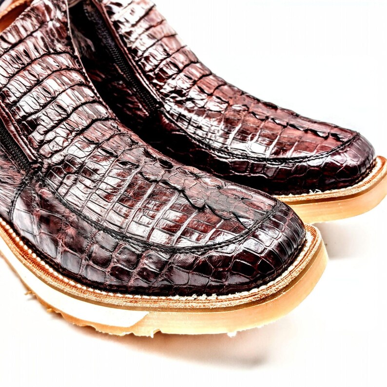 May include: Close-up of a pair of brown alligator skin slip-on shoes with a white rubber sole.