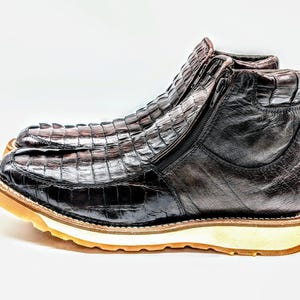 May include: Brown leather boots with a crocodile pattern and a white rubber sole. The boots have a zipper on the side and a pointed toe.