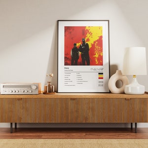 Op de afbeelding: Een ingelijst afdruk van een muziekalbumhoes met een rode en gele achtergrond. Het album heet "Clancy" en de artiest is "Twenty One Pilots". De albumhoes toont twee silhouetten die voor een vurige achtergrond staan. De afdruk bevat ook een tracklist en een kleine afbeelding van de Duitse vlag.