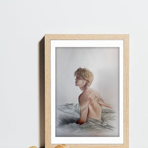 K&ouml;nnte beinhalten: Ein gerahmter Kunstdruck mit einer Bleistiftzeichnung einer Person mit blonden Haaren, die sitzt und zur Seite blickt. Das Kunstwerk befindet sich in einem hellen Holzrahmen mit neutralem Hintergrund.