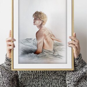 K&ouml;nnte beinhalten: Ein gerahmter Kunstdruck mit einer Bleistiftzeichnung einer Person mit blonden Haaren, die auf einem Bett sitzt. Das Kunstwerk befindet sich in einem goldenen Rahmen. Der R&uuml;cken der Person ist sichtbar, mit einem Tattoo. Das Kunstwerk wird von einer Person gehalten, die einen schwarz-wei&szlig;en Pullover tr&auml;gt.