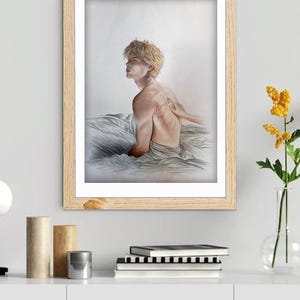 K&ouml;nnte beinhalten: Ein gerahmtes Kunstwerk mit einem Aquarellportr&auml;t einer Person mit blonden Haaren, die sitzt und zur Seite blickt. Das Kunstwerk befindet sich in einem hellen Holzrahmen und wird auf einem wei&szlig;en Schrank ausgestellt. Eine Hand ber&uuml;hrt den R&uuml;cken der Person. Rechts ist eine Vase mit gelben Blumen.