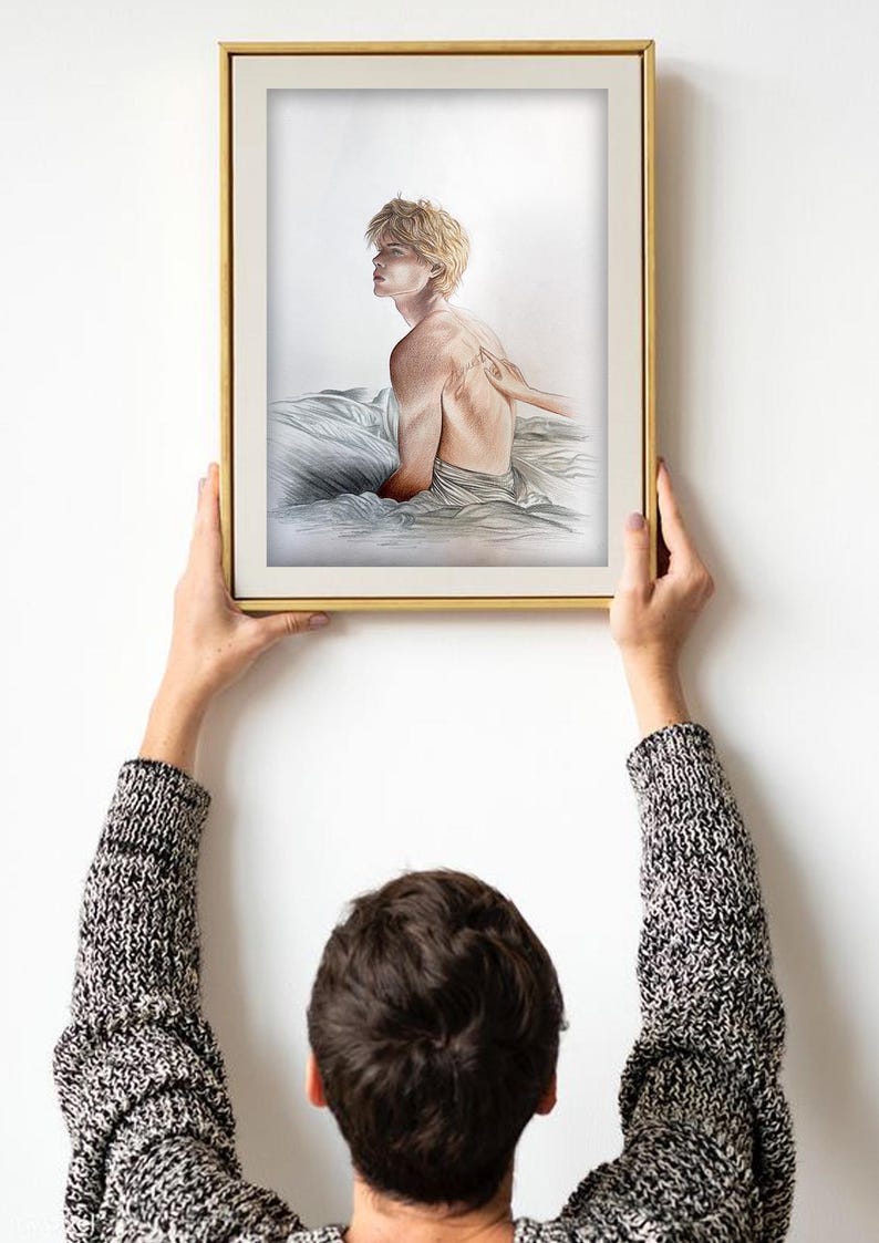 K&ouml;nnte beinhalten: Ein gerahmter Kunstdruck mit einer Bleistiftskizze einer Person mit kurzen blonden Haaren, die auf einem Bett sitzt. Die Person ist zur Seite gedreht, eine Hand ber&uuml;hrt ihren R&uuml;cken. Der Rahmen ist goldfarben.