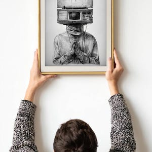 May include: Black and white art print of a person with a vintage radio and television in place of a head. The person is wearing a long-sleeved shirt and has their hands clasped in prayer. The artwork is framed in a gold-colored frame.